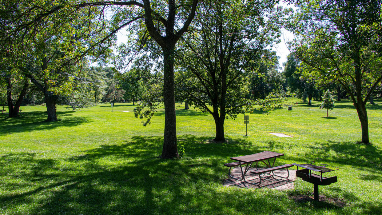 Sunlight and shadow highlight an empty picnic table and grill at a disc golf park in Ankeny, Iowa.