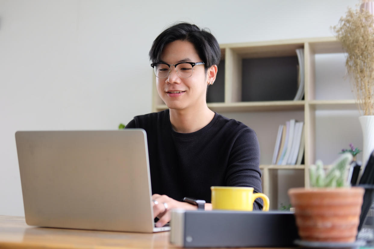 Smiling asian male working with laptop computer at creative office.