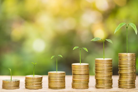 Coins stacked in increasing higher columns with seedlings sprouting from their top.