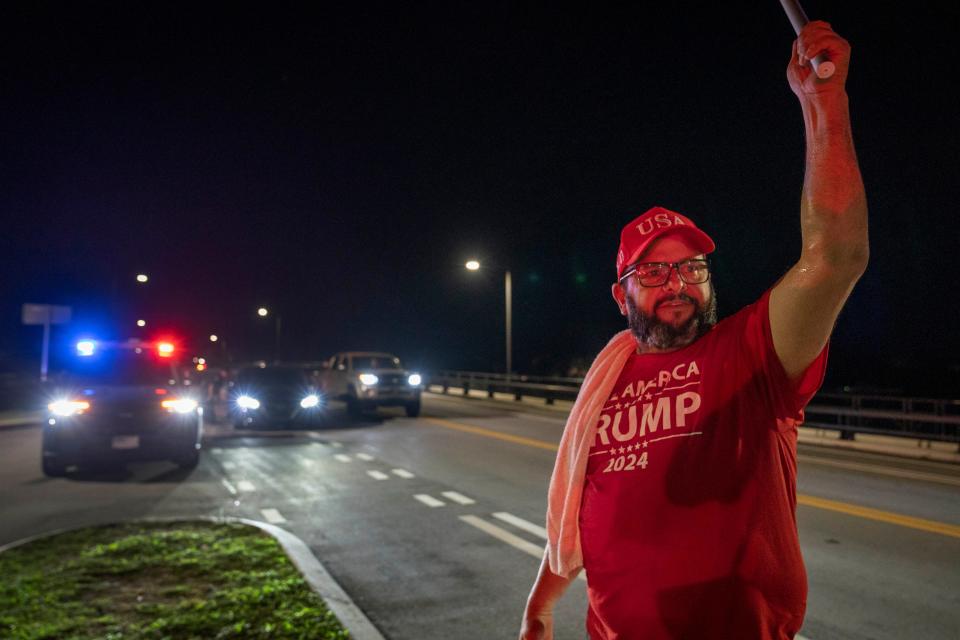 Trump supporter Joaquin Gutierrez waves a flag Saturday night across the bridge from Mar-a-Lago in a show of support for former President Donald Trump, who was slightly injured in a shooting at a rally in Pennsylvania earlier in the day.