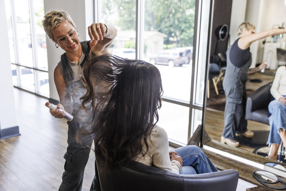 Hairdresser and small business owner spraying a customer's hair with hairspray
