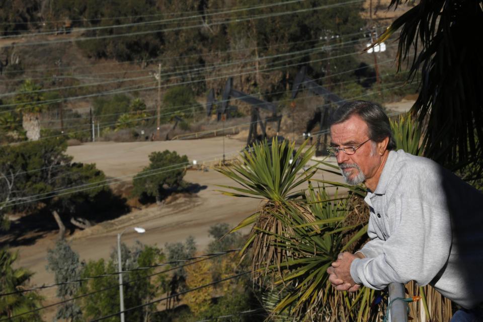 Homeowner Gary Gless leans over his balcony, as drilling wells are seen in the background, in Los Angeles