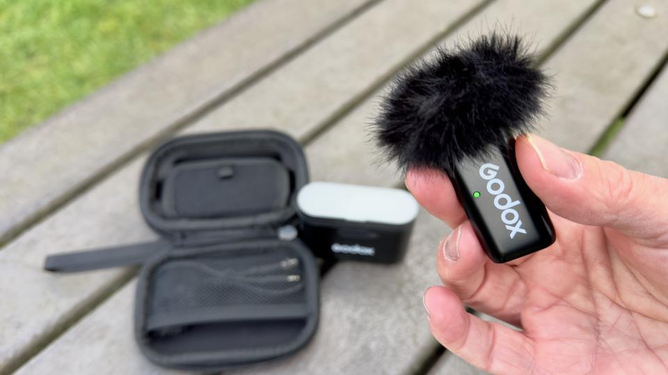 Hand holding a Godox WES2 Microphone with the case in the background