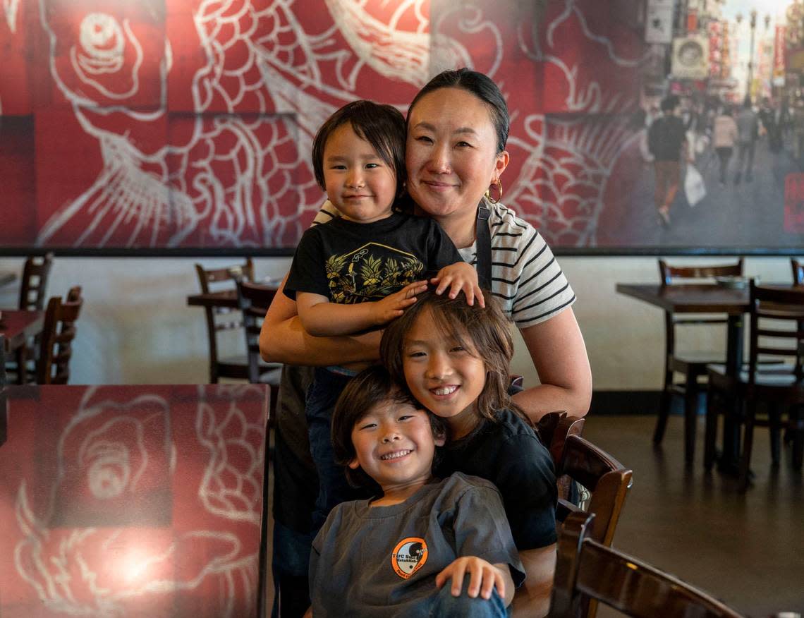 Toki Sawada, Binchoyaki chef and owner, stands with her three children, Yoshi, 3, left, Kiku, 9, and Haru Takehara, 5, bottom, at her restaurant Wednesday. She said she’s had to learn how to put her work schedule into children’s schedules to balance her life.