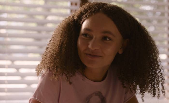 Joel's daughter Sarah in the series smiling while she's sitting in front of a window with blinds