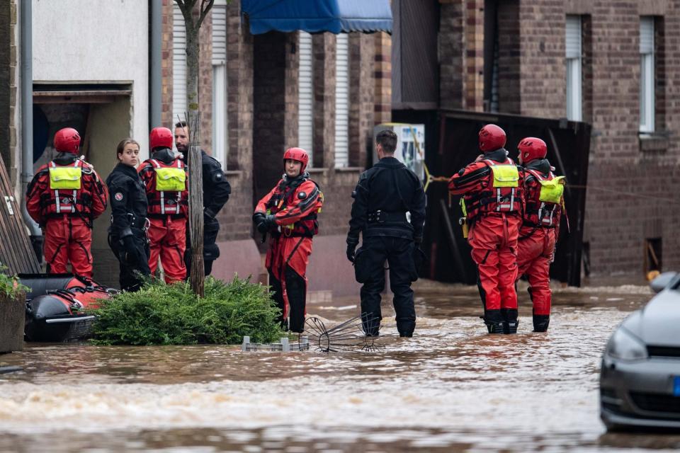 Rettungsschwimmer und Polizeitaucher stehen in einer überfluteten Straße in Erfstadt.