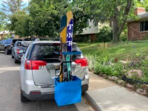 Blue Chuck Bucket ski carry system loaded with multiple pairs of skis and mounted on grey minivan on a neighborhood street