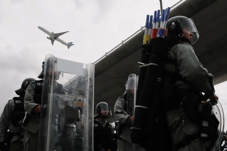 A plane flies over riot police during the anti-extradition bill protest outside the airport in Hong Kong