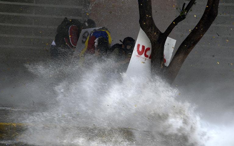 Anti-government activists protesting against Venezuelan President Nicolas Maduro take shelter behind a tree during clashes with the National Police, in Caracas, on March 20, 2014