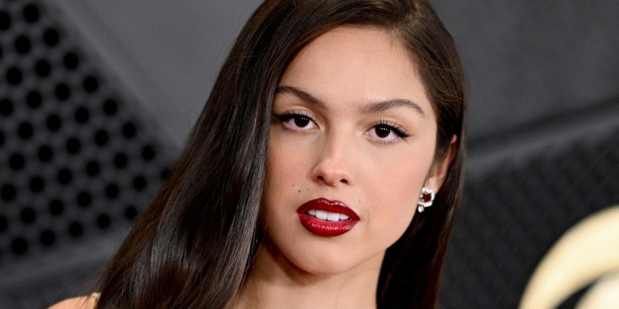 olivia rodrigo wears her hair down with a red lip and white strappy dress at the 66th grammy awards arrivals