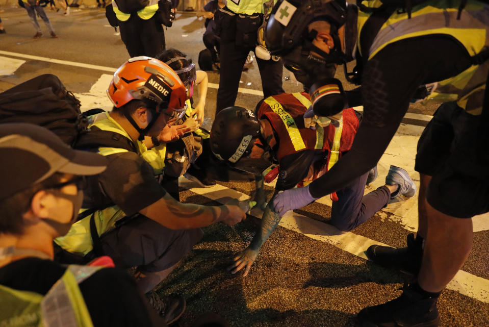 Medics treat a journalist who was injured in a protest in Hong Kong, Saturday, Sept. 28, 2019. Protesters streamed onto a main road nearby and some targeted government buildings that were barricaded. Police initially used a hose to fire pepper spray after some demonstrators threw bricks. A water cannon truck later fired a blue liquid, used to identify protesters, after protesters lobbed gasoline bombs through the barriers. (AP Photo/Vincent Thian)