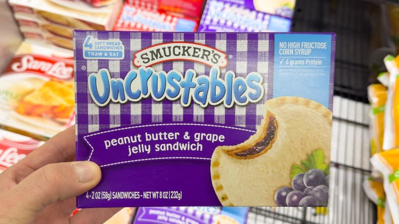 A hand holding a package of Smucker's Uncrustables