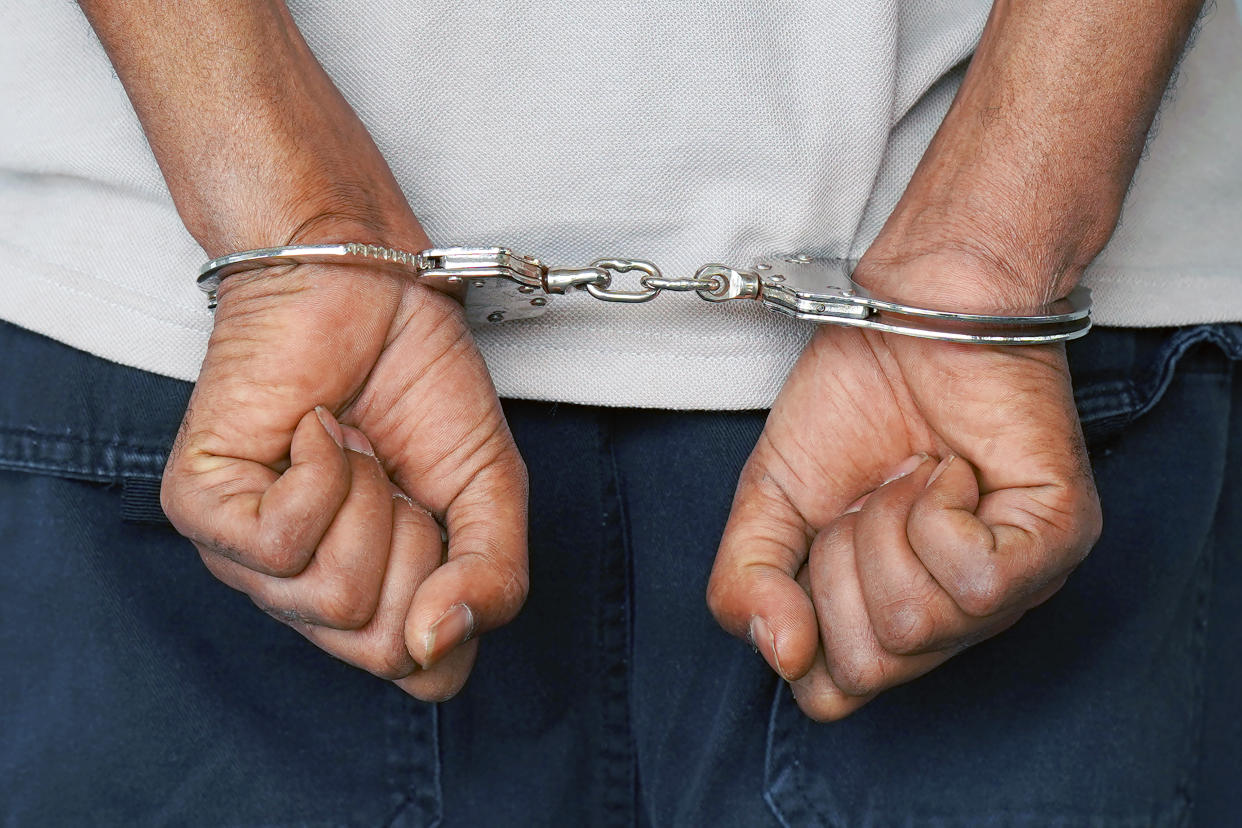 Close-up. Arrested man handcuffed hands at the back isolated on gray background. Prisoner or arrested terrorist, close-up of hands in handcuffs.