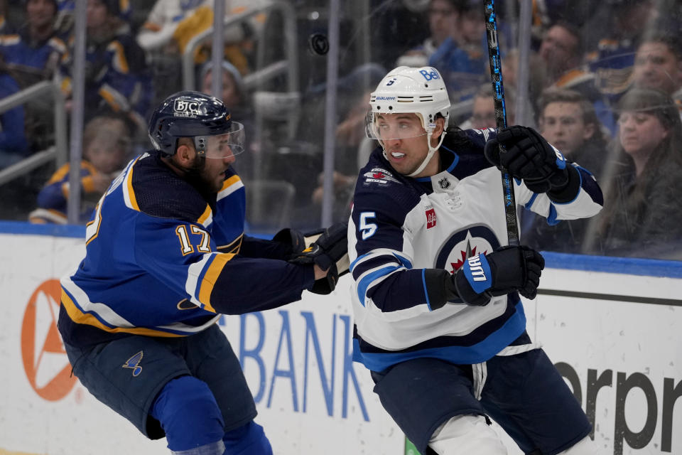 Winnipeg Jets' Brenden Dillon (5) and St. Louis Blues' Josh Leivo (17) battle for a loose puck during the second period of an NHL hockey game Sunday, March 19, 2023, in St. Louis. (AP Photo/Jeff Roberson)