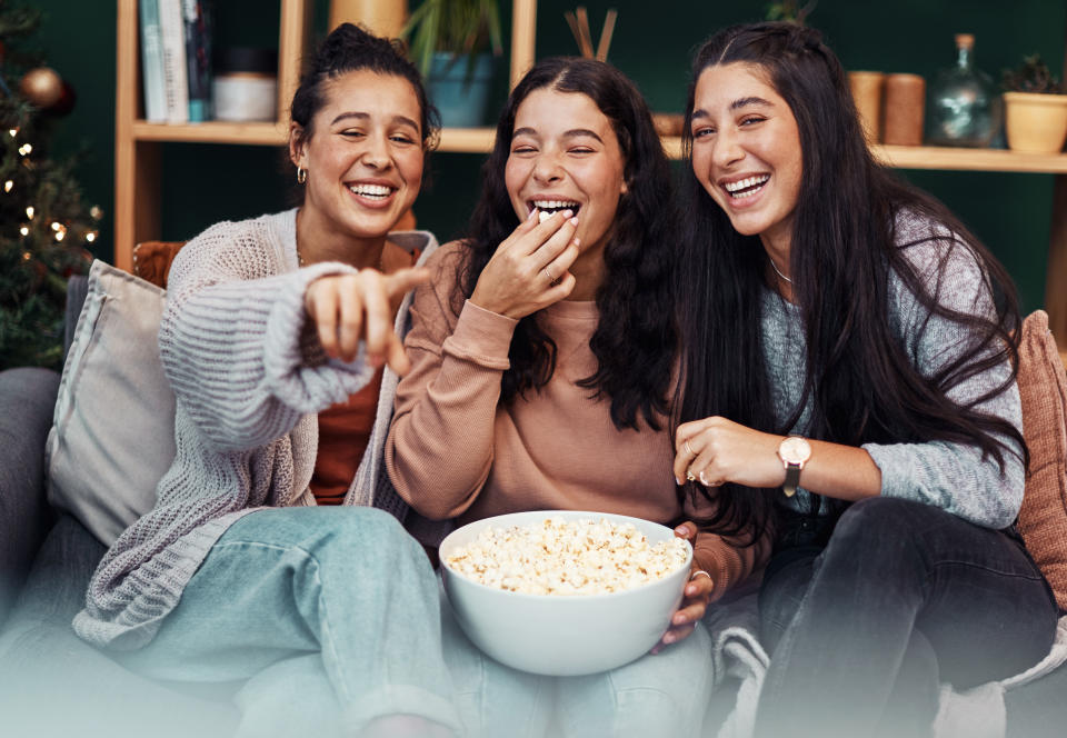 young women laughing and having popcorn together in front of the TV