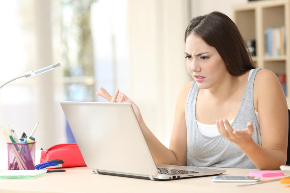 Woman sitting at a desk, looking confused and frustrated at her laptop with hands raised in questioning gesture