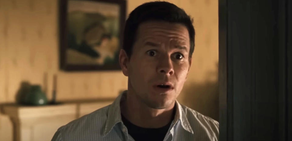 Mark Wahlberg looks surprised, standing indoors in front of a framed picture on the wall