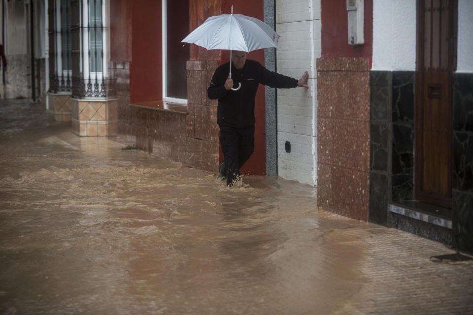 A man leans on a garage door for support while crossing a flood street in the village of Campillos, Spain, where heavy rain and floods have caused severe damage and the death of a firefighter according to Spanish authorities Sunday, Oct. 21 2018. Emergency services for the southern region of Andalusia say that the firefighter went missing when his truck overturned on a flooded road during heavy rains that fell through the night, and his body was found after a search Sunday morning.(AP Photo/Javier Fergo)