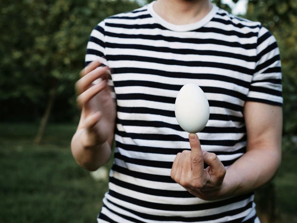 A man in a stripped shirt holds an egg balanced on the tip of his finger.