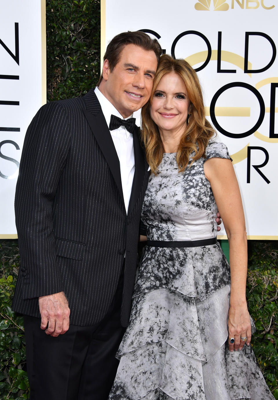 John Travolta in a pinstripe suit and Kelly Preston in a flowy black and white dress at the Golden Globe Awards