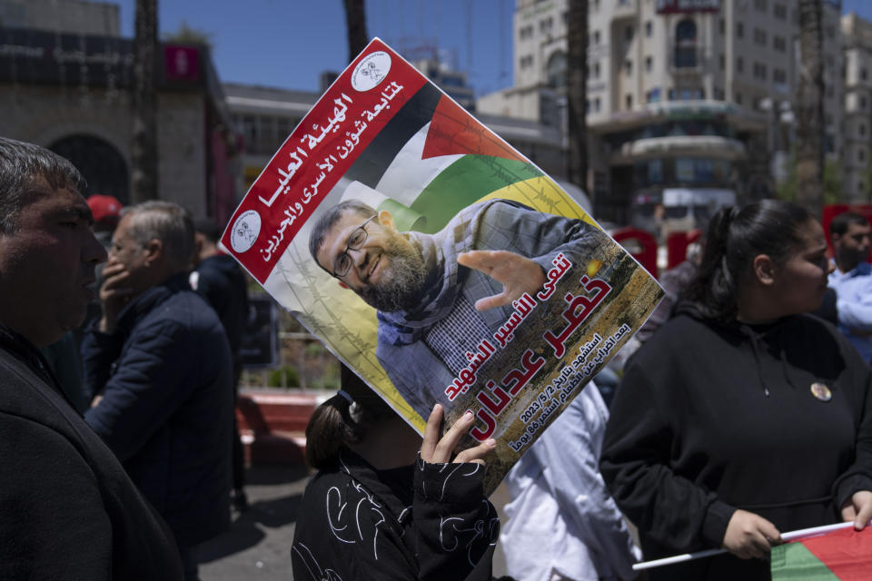 A Palestinian activist protects her head from the sun using a poster with name and picture of Khader Adnan, a leader in the militant Islamic Jihad group, and Arabic that reads "the high committee of the prisoners sends condolences, a martyr after an 86 days of hunger strike," during a protest in the West Bank city of Ramallah Tuesday, May 2, 2023. The high-profile Palestinian prisoner died in Israeli custody on Tuesday after a nearly three-month-long hunger strike, Israel's prison service announced. (AP Photo/Nasser Nasser)
