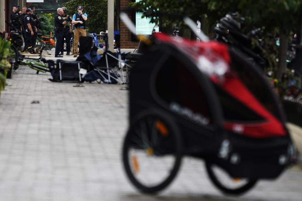 Police gather on a sidewalk lined with overturned chairs and abandoned strollers