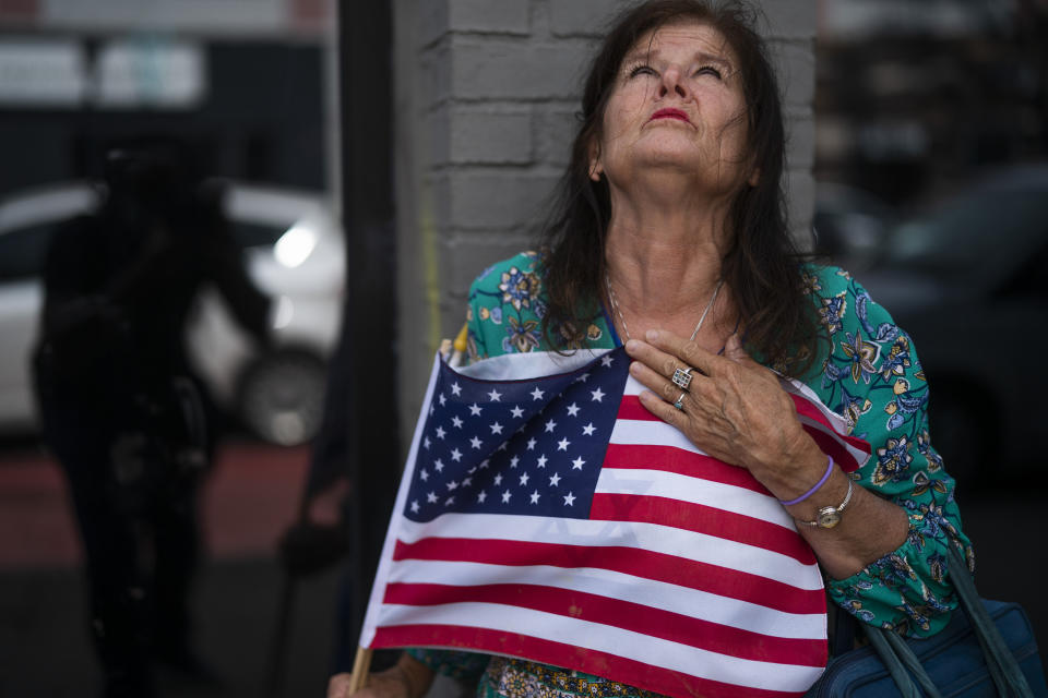 Merrilyn Downs clinches the U.S. flag at the site where a shooting happened in Minneapolis' Uptown neighborhood, Sunday, June 21, 2020. The shooting in the popular nightlife area early left one man dead and multiple people wounded in a chaotic scene that sent people ducking into restaurants and other businesses for cover. (Jerry Holt/Star Tribune via AP)