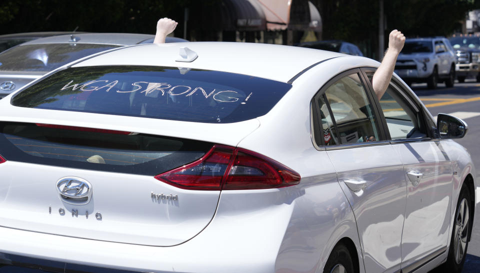 A car with "WGA Strong" written on the rear windshield, in support of the Writers Guild of America, drives past striking writers and actors outside Paramount studios in Los Angeles on Friday, July 14, 2023. This marks the first day actors formally joined the picket lines, more than two months after screenwriters began striking in their bid to get better pay and working conditions. (AP Photo/Chris Pizzello)