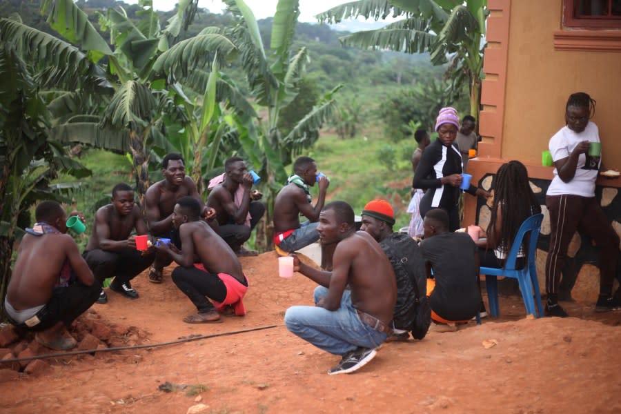 Ugandan youths have breakfast before an amateur wrestling tangle in the soft mud in Kampala, Uganda Wednesday, March. 20, 2023. The open-air training sessions, complete with an announcer and a referee, imitate the pro wrestling contests the youth regularly see on television. While a pair tangles inside the ring, made with bamboo poles strung with sisal rope, others standing ringside cheer feints and muscular shows of strength. (AP Photo/Patrick Onen)