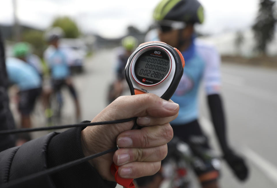 Wilson Sandoval, the manager of the Esteban Chaves Foundation cycling team, clocks his cyclists during time trial training in Puente Piedra near in Bogota, Colombia, Friday, Sept. 13, 2019. Although the team's cyclists are clean, Colombian cycling veteran Juan Pablo Villegas said in 2015 that the widespread use of performance enhancing drugs is driven by the desperate economic situation many of the country's 5,000 professional cyclists find themselves in. With little prize money available and most professional teams offering only minimal support, many will do whatever it takes to survive in the sport. (AP Photo/Fernando Vergara)