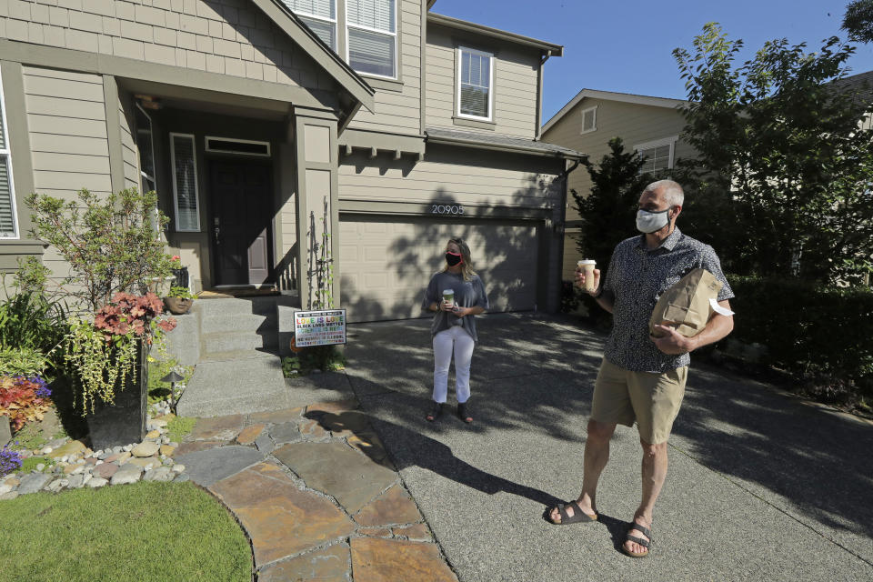 Julie and Greg Schwab stand in front of their home after walking back with their orders from the Dreamy Drinks and YS Street Food food trucks, Monday, Aug. 10, 2020, near the suburb of Lynnwood, Wash., north of Seattle. In June, Julie Schwab started organizing a regular schedule to bring food trucks to their neighborhood as a way to both help small businesses and give families staying at home during the coronavirus pandemic different options for meals. Long seen as a feature of city living, food trucks are now finding customers in the suburbs during the coronavirus pandemic as people are working and spending most of their time at home. (AP Photo/Ted S. Warren)