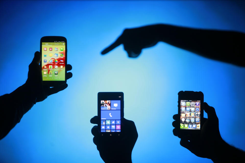 Men are silhouetted against a video screen as they pose with Samsung Galaxy S3, Nokia Lumia 820 and iPhone 4 smartphones (L-R) in this photo illustration taken in the central Bosnian town of Zenica, May 17, 2013. REUTERS/Dado Ruvic (BOSNIA AND HERZEGOVINA - Tags: BUSINESS TELECOMS)