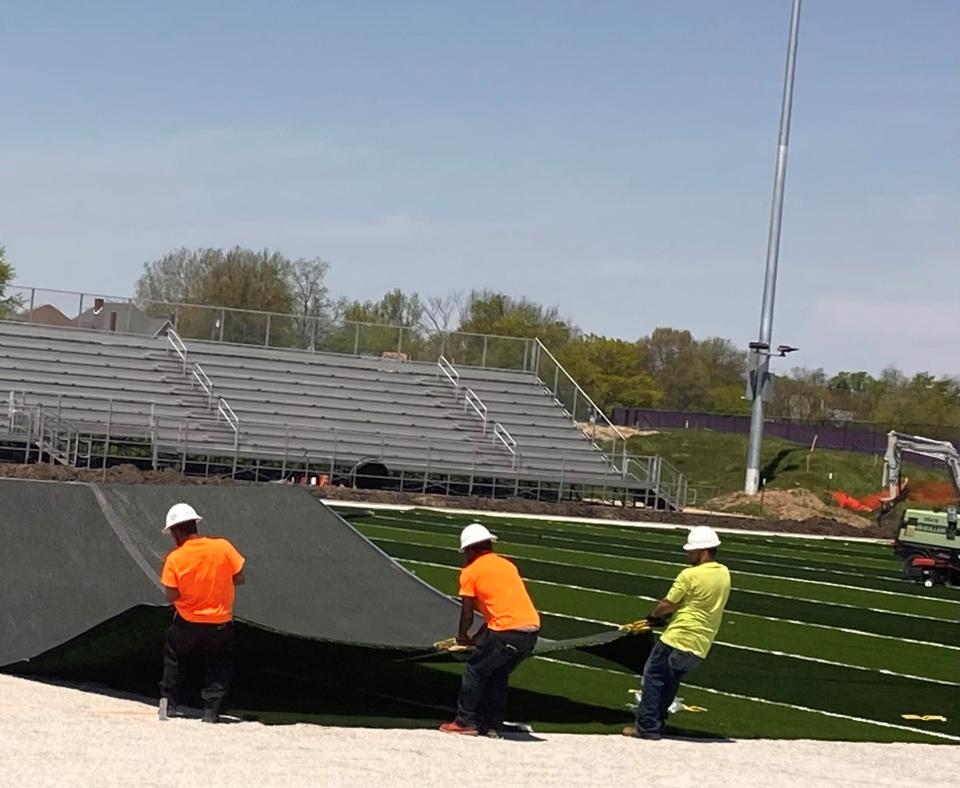 Workers rug on new artificial turf being laid on the new football field at Muncie Central High School. The project to replace the old stadium, located between the school and the Muncie Fieldhouse, is on target to be completed in early August.
