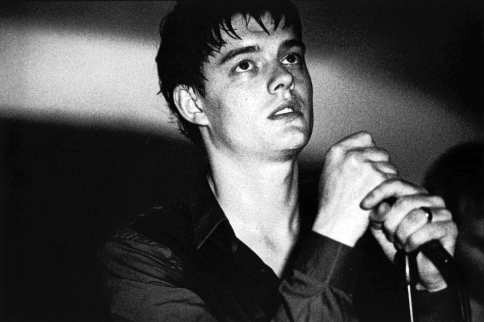 Sam Riley dressed like Ian Curtis and holding a mic