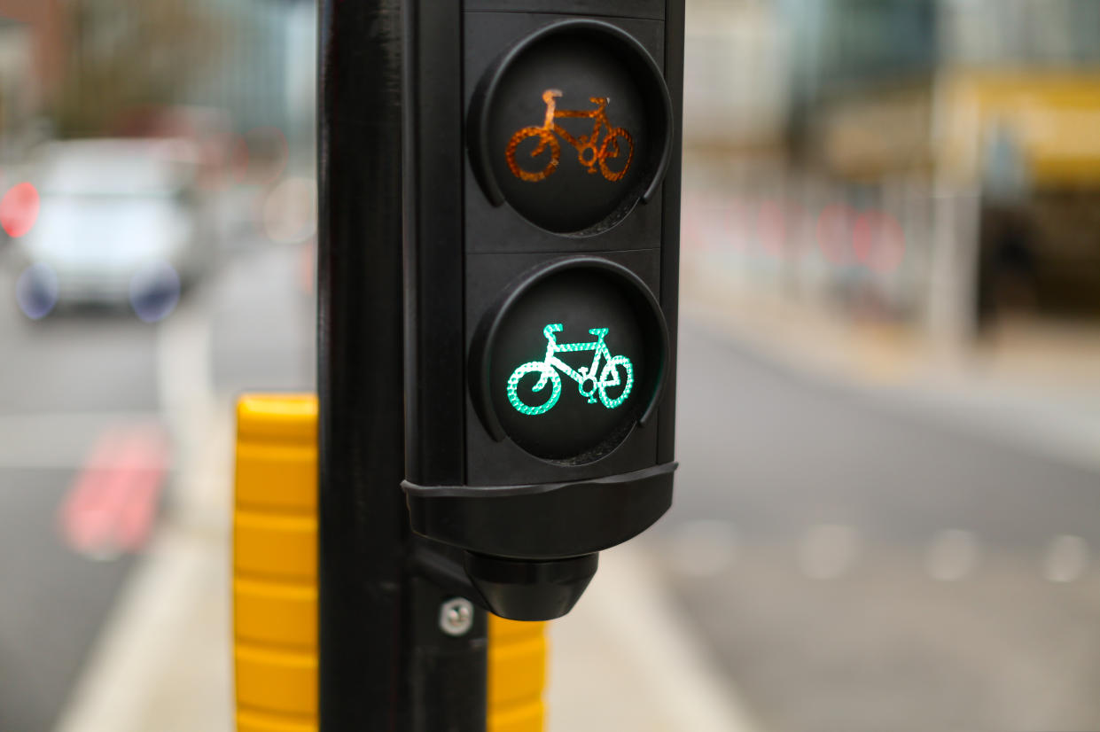 A London traffic light for bicycles showing a green light, the background shows the road ahead out of focus