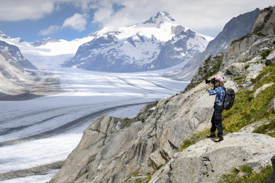 FILE - In this July 21, 2020 file photo, Swiss photographer David Carlier takes photographs of the Swiss Aletsch glacier, the longest glacier in Europe, on the sideline of his photographic exhibition, in Fieschertal, Switzerland. Climate change is increasingly damaging the U.N.’s most cherished heritage sites, a leading conservation agency warned Wednesday Dec. 2, 2020, reporting that Australia’s Great Barrier Reef and dozens of other natural wonders are facing severe threats. (Laurent Gillieron/Keystone via AP, File)