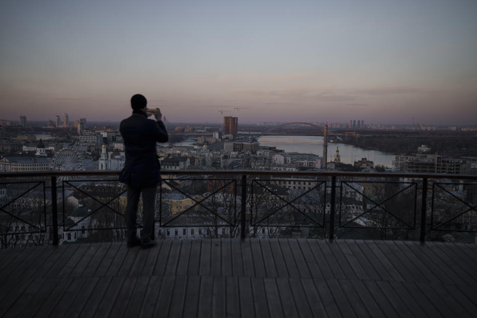A man takes photos with his phone as the sun sets in Kyiv, Ukraine, Monday, March 14, 2022. (AP Photo/Felipe Dana)