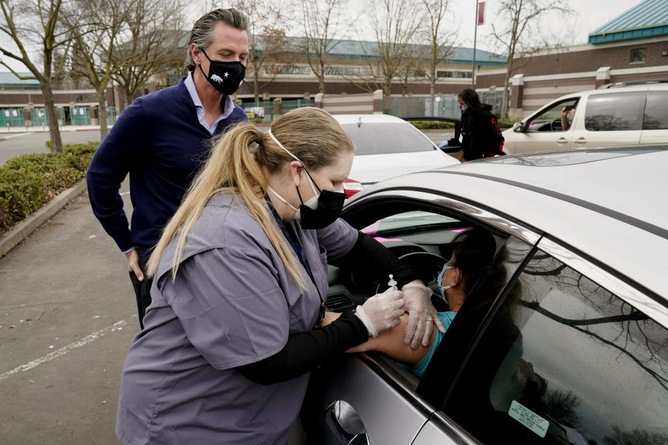FILE — California Gov. Gavin Newsom watches as LVN Cari Elkins administers a COVID-19 vaccination at a drive-thru vaccination center at Natomas High School on Feb. 11, 2021, in Sacramento, Calif. On Monday, Oct. 17, 2022, Both Newsom, a Democrat and Florida Gov. Ron DeSantis a Republican said their reelection victories were in part because of their commitment to freedom. But the governors have vastly different definitions of what freedom means. (AP Photo/Rich Pedroncelli,File)
