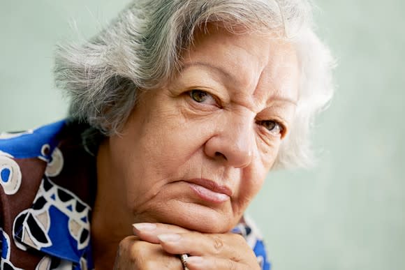 A senior woman in deep thought with her head resting on her interlocked hands.