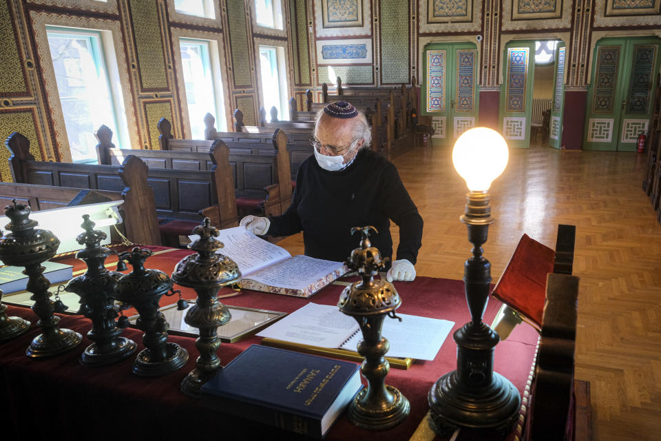 In this Wednesday, April 8, 2020 photo Jakob Finci, the President of the Jewish Community of Bosnia, looks at a religious book inside the synagogue in Sarajevo, Bosnia, as worshipers stay away due to the national lockdown the authorities have imposed attempting to limit the spread of the new coronavirus. (AP Photo/Kemal Softic)