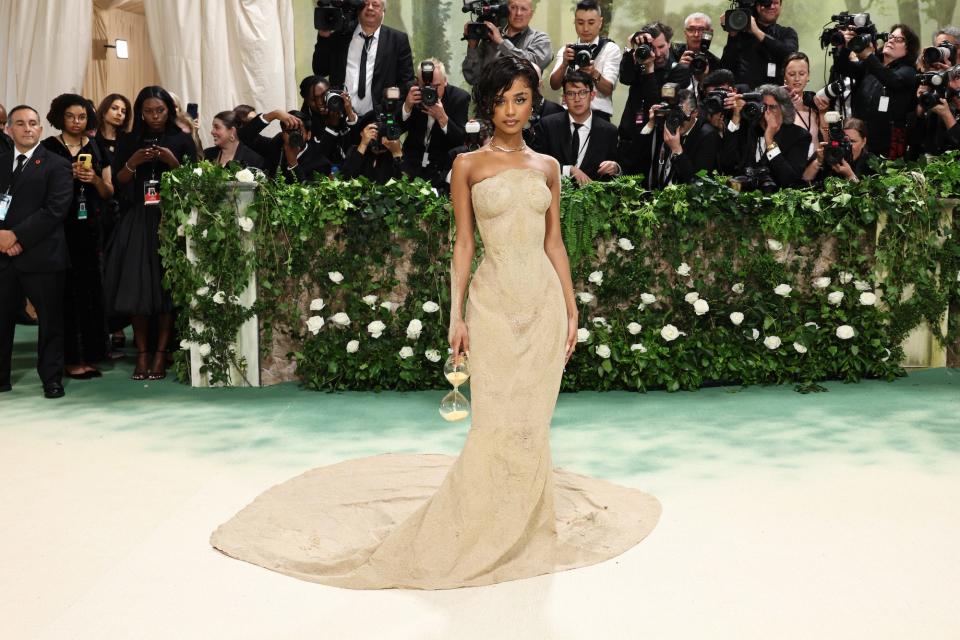 Tyla poses in front of photographers at the 2024 Met Gala, wearing a Balmain dress made out of sand and carrying an hourglass.