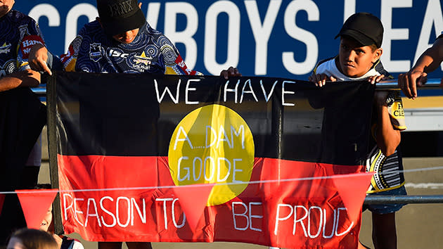 Kids with an Aboriginal flag emblazoned with the words 'We have reason to be proud'.