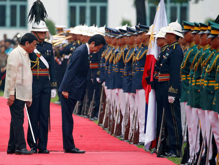 Japanese Prime Minister Shinzo Abe bows his head before the Philippine flag during a welcome ceremony at the presidential palace in Manila, Philippines January 12, 2017. REUTERS/Erik De Castro