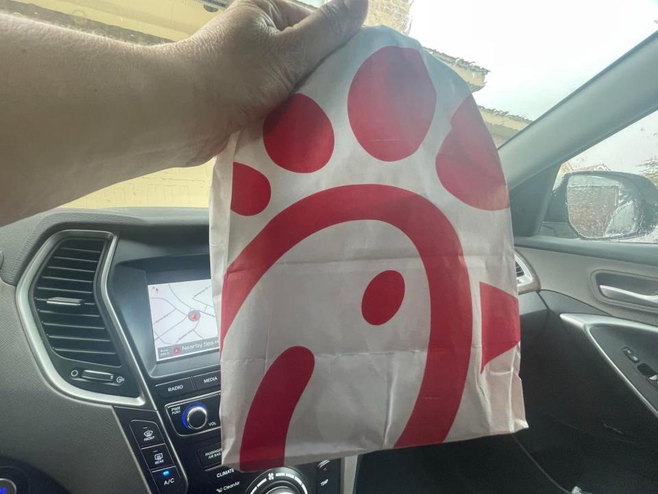 The writer holds a bag with Chick-fil-A logo on it in a car