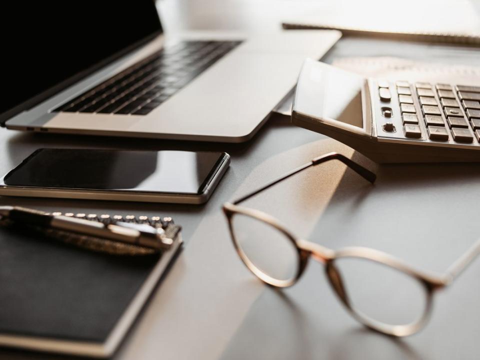 Place of work in office, calculator, laptop computer, glasses at office desk