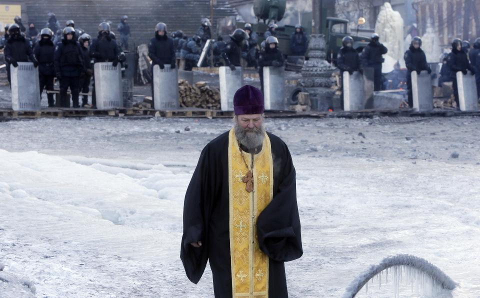 An Orthodox priest goes between riot police and opposition activists' barricades in central Kiev, the epicenter of the country's current unrest, Ukraine, Sunday, Feb. 2, 2014. Kitted out in masks, helmets and protective gear on the arms and legs, radical activists are the wild card of the Ukraine protests now starting their third month, declaring they're ready to resume violence if the stalemate persists.(AP Photo/Efrem Lukatsky)