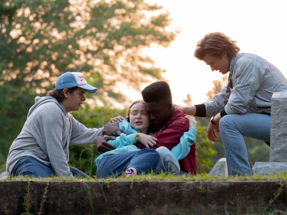 A scene from "Stranger Things" season four showing Dustin, Max, Lucas, and Steve (four teenagers) in a group hug.