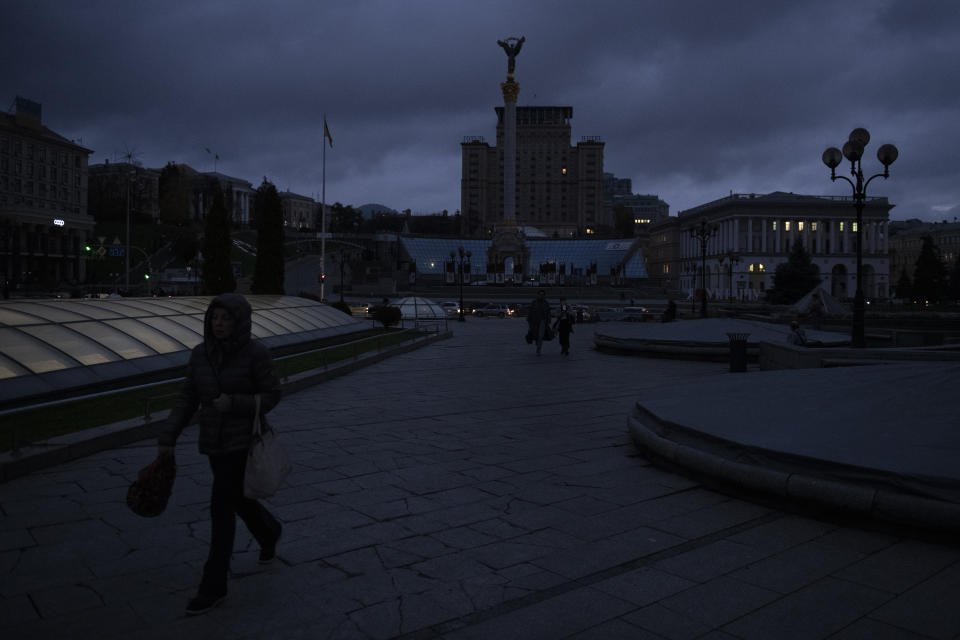 People walk in Independence Square at twilight in Kyiv, Ukraine, Monday, Oct. 31, 2022. Rolling blackouts are increasing across Ukraine as the government rushes to stabilise the energy grid and repair the system ahead of winter. (AP Photo/Andrew Kravchenko)