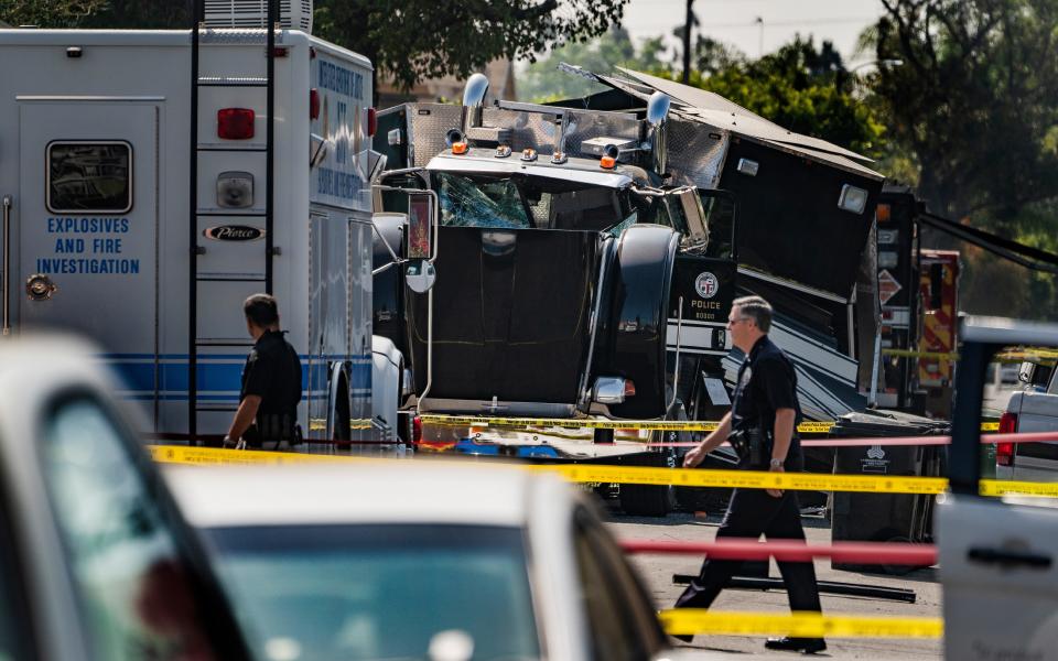 Police officers walk past the remains of an armored Los Angeles Police Department tractor-trailer after illegal fireworks seized at a home exploded in South Los Angeles.