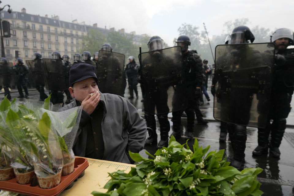 A man sells the traditional Lily of the Valley as riot police officers stand behind him during a demonstration, Monday, May 1, 2023 in Paris. Across France, thousands marched in what unions hope are the country's biggest May Day demonstrations in years, mobilized against President Emmanuel Macron's recent move to raise the retirement age from 62 to 64. (AP Photo/Thibault Camus)